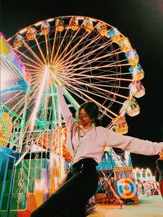 a woman posing in front of a ferris wheel at an amusement park with her arms outstretched