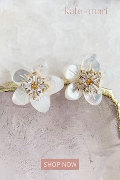 two white flowers on a gold branch with crystal stones in the center and text, kate - mari shop now