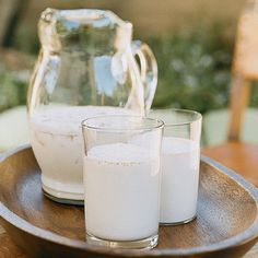 there are two glasses and pitcher on the table next to each other, one is filled with milk