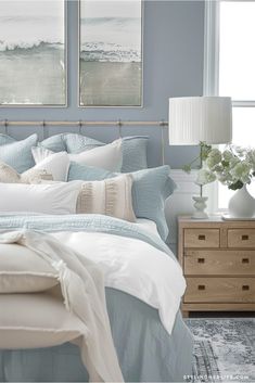 a bedroom with blue walls and white bedding, two paintings on the wall above the bed