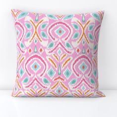 a pink and blue pillow with an abstract design on the front, sitting on a white surface