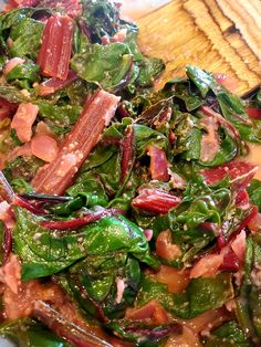 a salad with spinach, ham and other vegetables on a white plate next to a wooden utensil