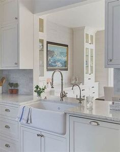 a kitchen with white cabinets and marble counter tops, an island style sink in the center