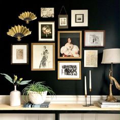 a black wall with many pictures on it and a lamp next to the table in front of it