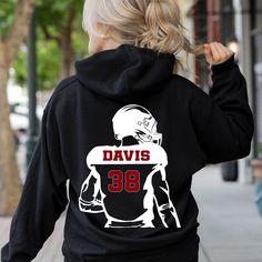 This sweatshirt can be customized with your school colors and mascot, along with the player's name and number. This football hoodie has a design on the front and back.  Custom football sweatshirt with your player's name, number, school colors and mascot.  Perfect for football moms on cold game nights.   Please refer to the sizing chart in the photo. For an oversized sweatshirt, choose one at least 2-3 sizes larger that you would normally wear For more school spirit designs, click here: https://www.etsy.com/shop/JLsTshirts?ref=seller-platform-mcnav§ion_id=36596774 For other Tshirts, check out my full shop: https://www.etsy.com/shop/JLsTshirts * Adult Unisex Hooded Sweatshirt, Gildan * Drawstring hood, spacious pockets * Soft, comfortable feel * 50% cotton, 50% polyester * Medium-heavy fabri Custom Basketball Hoodie, Football Hoodies, Basketball Hoodie, Basketball Sweatshirts, Football Sweater, Football Mom Shirts, Football Gift, Custom Basketball, Mom Hoodies