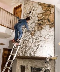 a man climbing up the side of a ladder to paint a stone wall in a living room