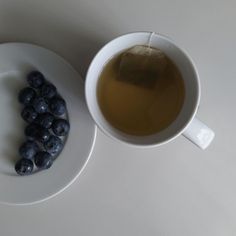 a white plate topped with blueberries next to a cup of tea