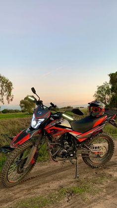 a dirt bike parked on top of a dirt road next to a lush green field