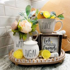 three teapots with lemon slices and flowers in them on a tray next to a tile wall