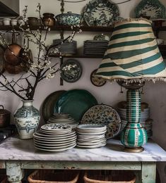 a table topped with lots of plates and vases next to a shelf filled with dishes