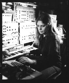 black and white photograph of woman working on electronic equipment in recording studio with sound board