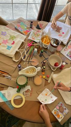 two women sitting at a table with art supplies and paper work on the table next to them