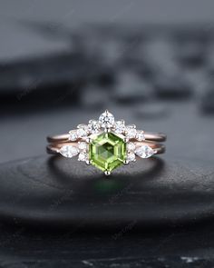 an engagement ring with a green stone surrounded by white diamonds on top of a black surface