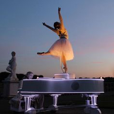 a woman in a white dress is standing on top of a piano with her arms outstretched