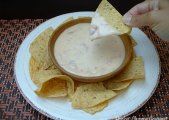 a person dipping tortilla chips into a white bowl filled with quesadilla dip