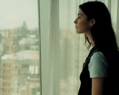 a woman standing in front of a window looking out at the city