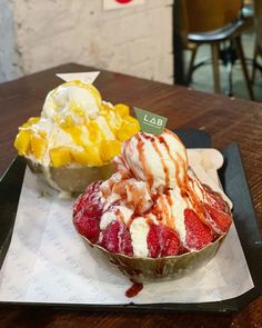 two desserts are sitting on a tray at a restaurant, one is covered in ice cream and the other has fruit