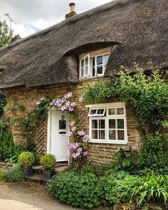 an old thatched house with flowers growing on the front door and windows, surrounded by greenery