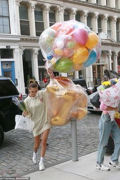 two women are walking down the street with large balloons on their head and one is carrying bags