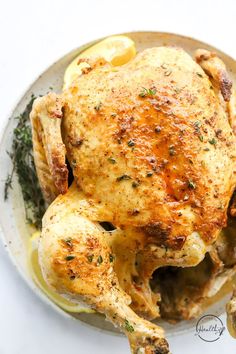 a whole chicken on a plate with lemons and herbs