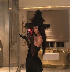 a woman in a black dress and hat taking a selfie