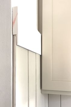 a close up of a white kitchen cabinet door with a mirror on the wall above it