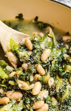 broccoli and white beans are mixed together in a pot with a wooden spoon