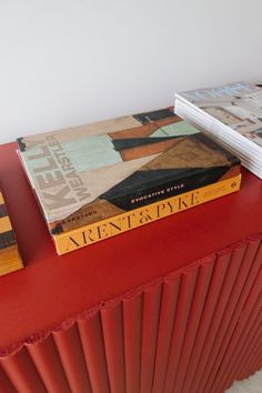 two books sitting on top of a red table next to each other in front of a white wall