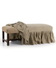 a bed with a ruffled cover on it and a wooden foot rest in the middle