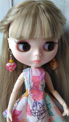 a close up of a doll with long blonde hair and big eyes wearing a dress