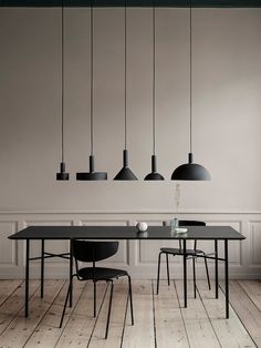 a dining table with four chairs and five lights hanging from the ceiling above it, in an empty room