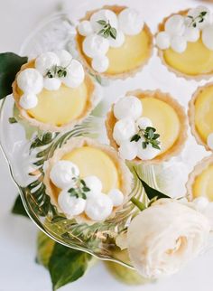 small desserts are arranged on a glass platter with flowers and leaves around them