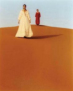 two women in white dresses walking across a desert