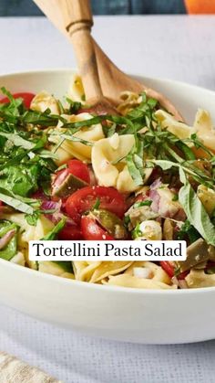 a white bowl filled with pasta and veggies next to a wooden spatula