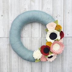 a yarn wreath decorated with flowers on a white wooden background, ready to be used as a decoration