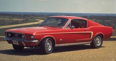 an old red mustang sitting on the side of a road