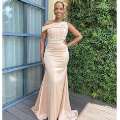 a woman standing in front of a green wall wearing a nude colored gown with an off the shoulder neckline