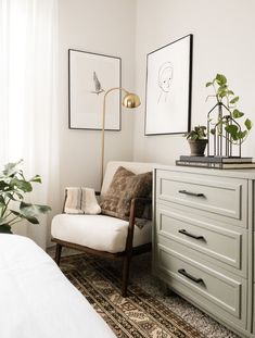 a white chair sitting next to a dresser in a room with plants on top of it