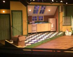 an empty stage set for a play with green doors and white appliances on the floor