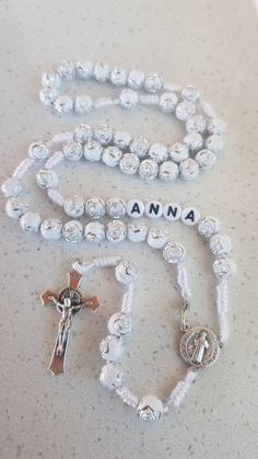 Custom rosary with name. This rosary is made on very resist cord. It is made with white rose-shaped beads with silver details. In this rosary there is hook so that this rosary you can wear it around the neck. Beads size is 8 mm. Cross and medal material: metal. Cord cotton. The rosary is made of very high quality so that you and your loved ones will be able to enjoy it for a long time. Centerpiece and cross is Saint Benedict. Metal parts made in Italy. Product color may slightly vary due to phot Adjustable White Rosary For First Communion, White Beaded Cross Rosary, White Beaded Cross-shaped Rosary, White Rosary With 8mm Beads Crucifix, Handmade White Spiritual Rosary, Adjustable White Rosary As Gift, Personalized White Cross Rosary Bracelet, Personalized White Rosary, Our Lady Of Medjugorje