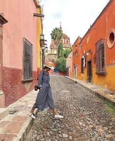 a woman walking down a cobblestone street in an old european town with colorful buildings