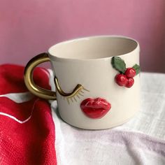 a white cup with cherries on it and a gold handle sitting on a table