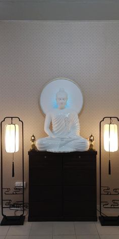 a buddha statue sitting on top of a black cabinet next to two lamps and a mirror