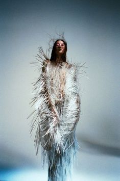 a woman is standing with her arms wrapped around her body and hair blowing in the wind