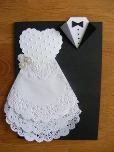 a wedding card with a white dress and tuxedo on it, sitting next to a black piece of paper