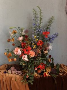 a vase filled with lots of colorful flowers on top of a cloth covered tablecloth