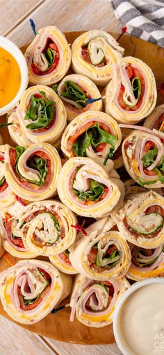 a platter filled with sandwiches and dips on top of a wooden table next to a bowl of dipping sauce