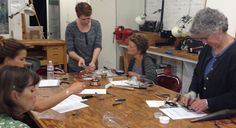 a group of women sitting around a wooden table working on crafts with scissors and glue