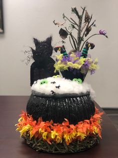 a black cat sitting on top of a pot filled with fake flowers and bats in it