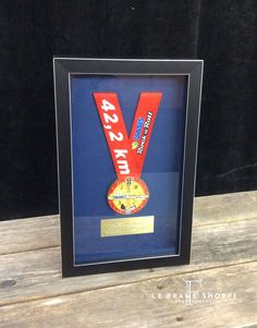 a framed medal is sitting on a wooden table next to a black frame with a red ribbon around it